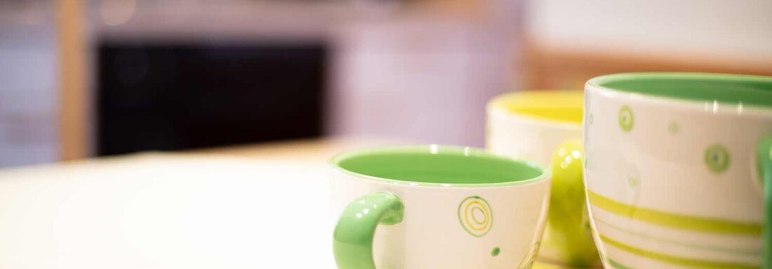 A selection of colorful mugs on a bright surface. In the background, a kitchen is visible. - Haus Sonnwend - Sölden