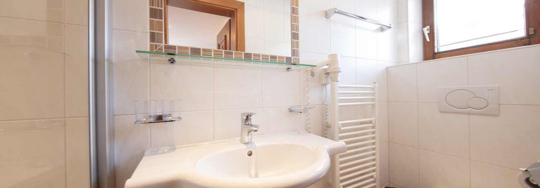 A modern bathroom with white tiles and natural light. It features a sink, a toilet, and a towel radiator. - Haus Sonnwend - Sölden