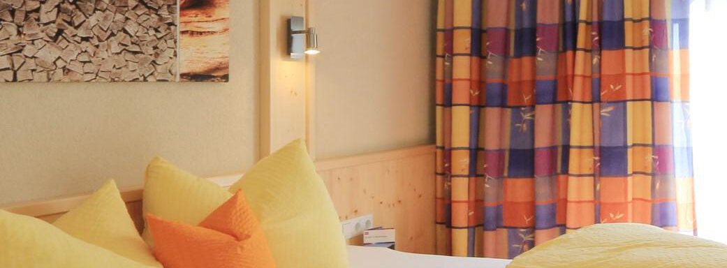 A cozy bedroom with a large bed and colorful pillows. The curtains are vibrant and give the room an inviting atmosphere. - Haus Stefanie - Sölden