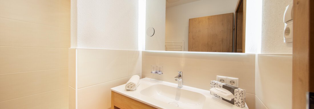 A modern bathroom with a stylish sink and gentle lights. Towels are neatly arranged on a wooden shelf. - Haus Stefanie - Sölden