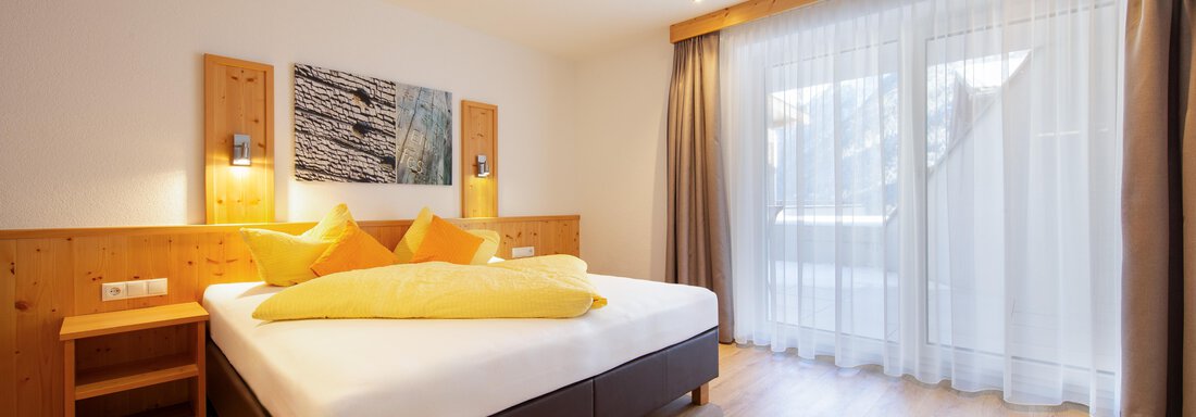A bright and modern bedroom with a large bed and colorful pillows. Large windows let in plenty of daylight and provide access to a balcony. - Haus Stefanie - Sölden