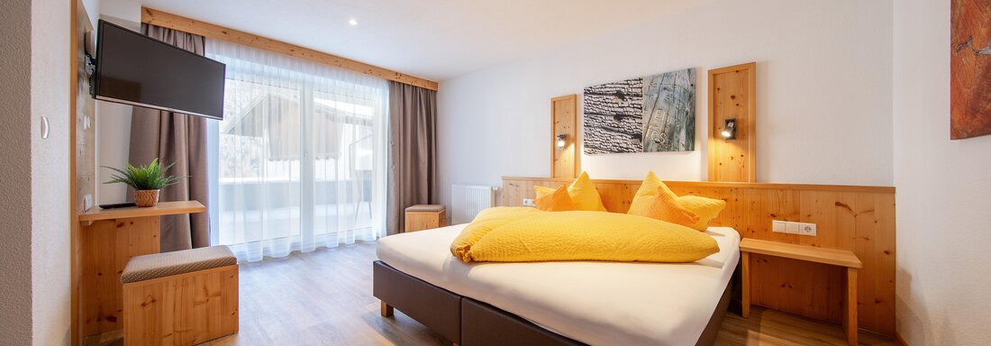 A modern room with a double bed, light walls, and warm wooden furniture. Large windows provide plenty of natural light and a cozy atmosphere. - Haus Stefanie - Sölden