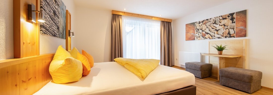 A modern bedroom with a large bed and colorful cushions. A cozy atmosphere with wooden colors and natural elements. - Haus Stefanie - Sölden