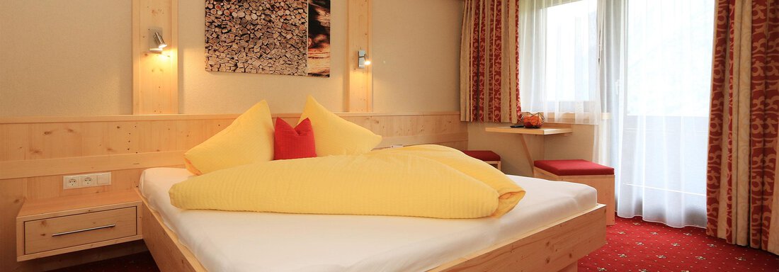 A cozy room with a large bed and colorful pillows. Large windows provide plenty of daylight and a view outside. - Haus Stefanie - Sölden