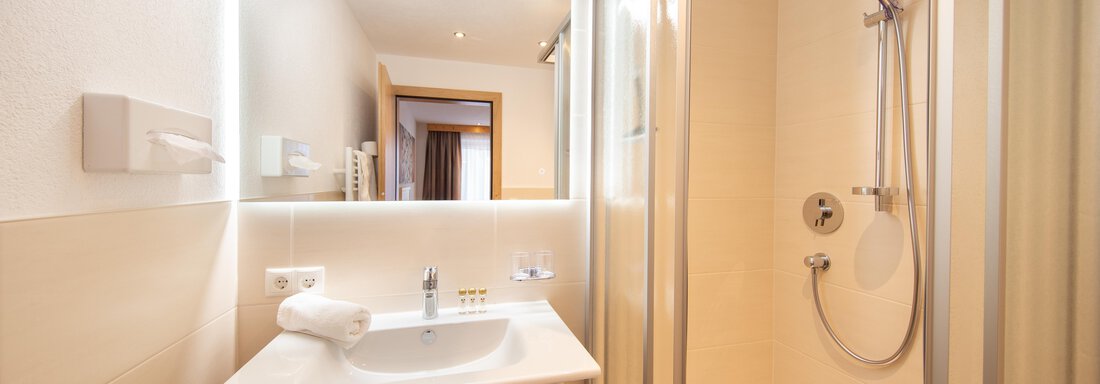 A modern bathroom with a sink, a shower, and a large mirror. The walls are bright, and the space feels clean and inviting. - Haus Stefanie - Sölden