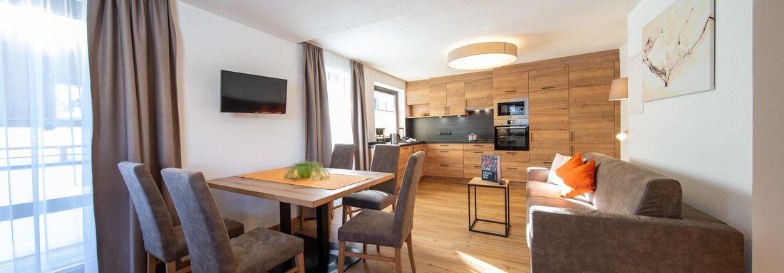 A modern living room with a dining table and several chairs. The decor is cozy and bright, with large windows that let in a lot of light. - Haus Stefanie - Sölden