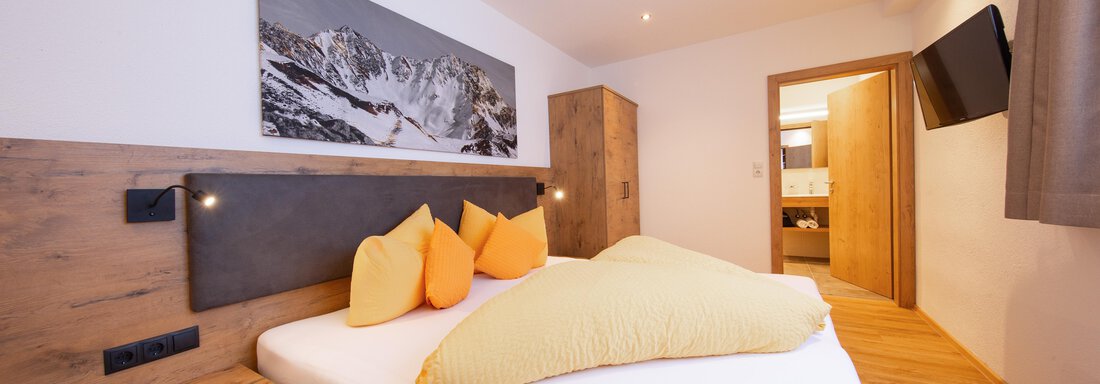 App. 16 A cozy bedroom with a large bed and colorful pillows. With wooden paneling and a beautiful picture on the wall, the room offers an inviting atmosphere. - Haus Stefanie - Sölden