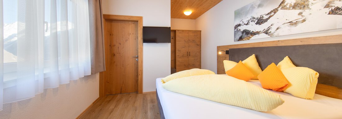 A modern bedroom with a large bed and colorful pillows. The room has a wooden ceiling and large windows that let in plenty of light. - Haus Stefanie - Sölden
