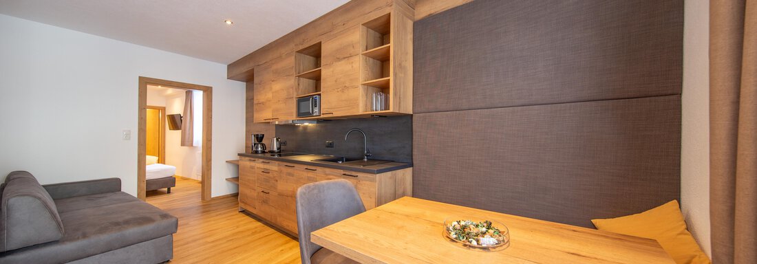 A modern kitchen with wooden shelves and a dining area. The room is bright and inviting, with a cozy sofa and a wooden floor. - Haus Stefanie - Sölden