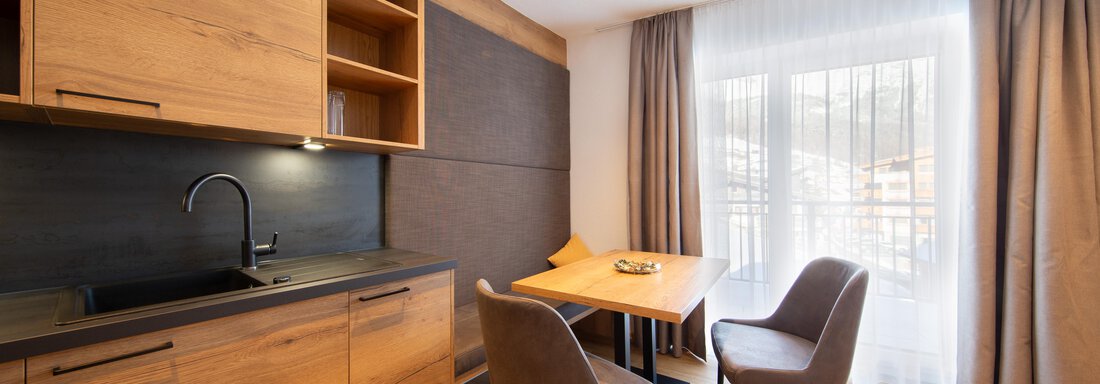 A modern kitchen nook with wooden cabinets and a minimally designed table. Two chairs are placed around the table, while daylight streams in through the windows. - Haus Stefanie - Sölden