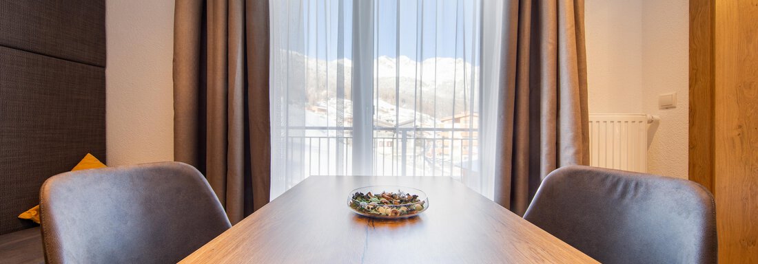A modern dining area with a wooden table and cozy chairs. In front of the window is a great view of the mountains. - Haus Stefanie - Sölden