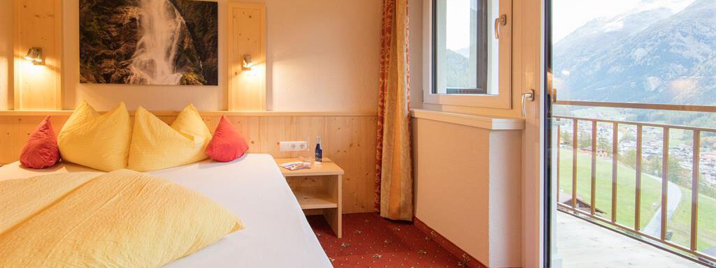 Doppelzimmer A cozy hotel room with a large bed and colorful cushions. The window offers a beautiful view of the mountains. - Haus Stefanie - Sölden