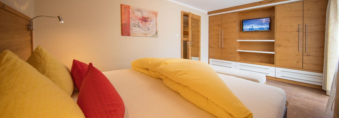 A cozy bedroom with a large bed and colorful pillows. A picture hangs on the wall and a TV is in the cupboard. - Haus Stefanie - Sölden