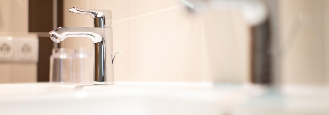 A modern sink with shiny faucets. In the background, bright tiles and a glass carafe are visible. - Haus Stefanie - Sölden