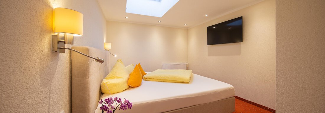 A cozy bedroom with a large bed and colorful pillows. The walls are bright and there is a television on the wall. - Haus Stefanie - Sölden