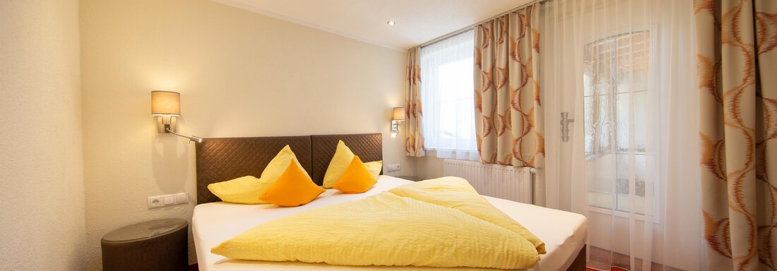 A cozy bedroom with a double bed and yellow pillows. Bright walls and windows create a friendly atmosphere. - Haus Stefanie - Sölden