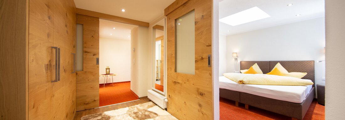 An inviting hallway with wooden walls and a friendly carpet. In the background, a bright bedroom with a double bed and yellow pillows can be seen. - Haus Stefanie - Sölden