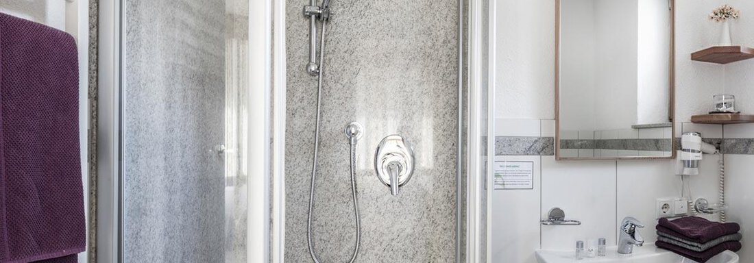 A modern bathroom with a shower and a sink. The walls are tiled in light colors, and there are towels in dark purple. - Haus Tanja - Sölden