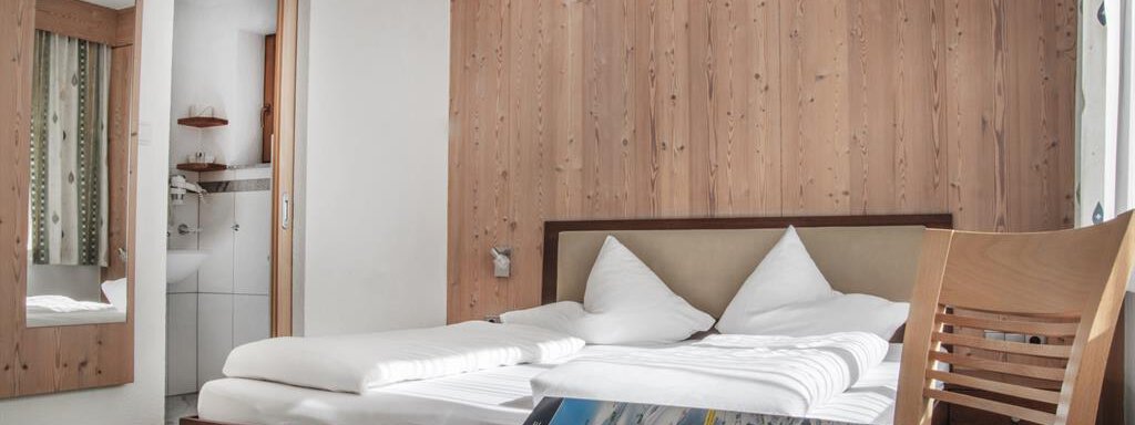 Doppelzimmer A cozy guest room with wooden paneling and a double bed. On the table lies a brochure with information about the surroundings. - Haus Tanja - Sölden