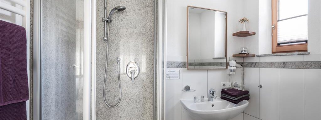 A modern bathroom with a shower and a sink. The walls are brightly tiled, and there is a large window front for natural light. - Haus Tanja - Sölden