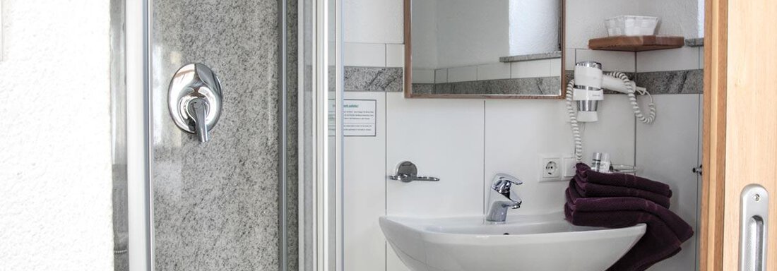 A modern bathroom with a shower, a sink, and a mirror. Towels are neatly placed on a shelf. - Haus Tanja - Sölden