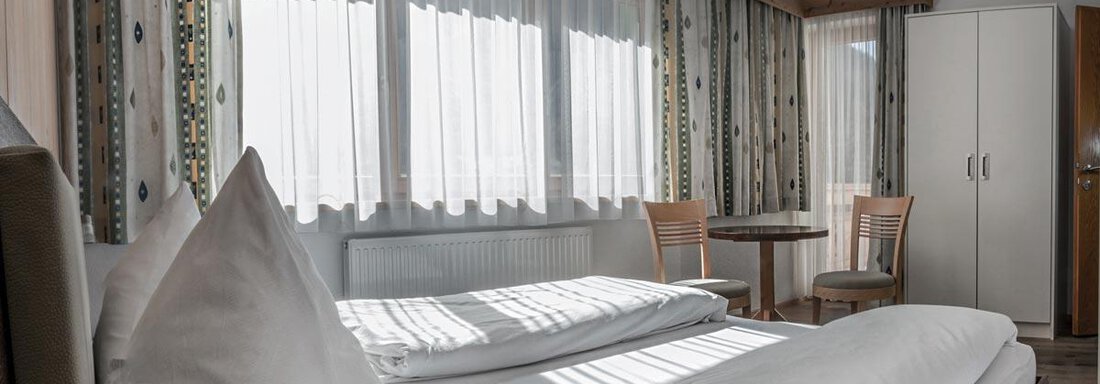 A cozy hotel room with a double bed and bright curtains. A table and two chairs complement the furnishings. - Haus Tanja - Sölden
