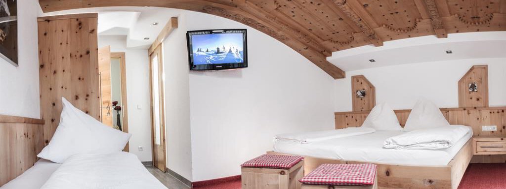 Dreibett Zirbe A cozy room with wooden elements and a red carpet. There are two beds, a television, and an inviting atmosphere. - Haus Tanja - Sölden