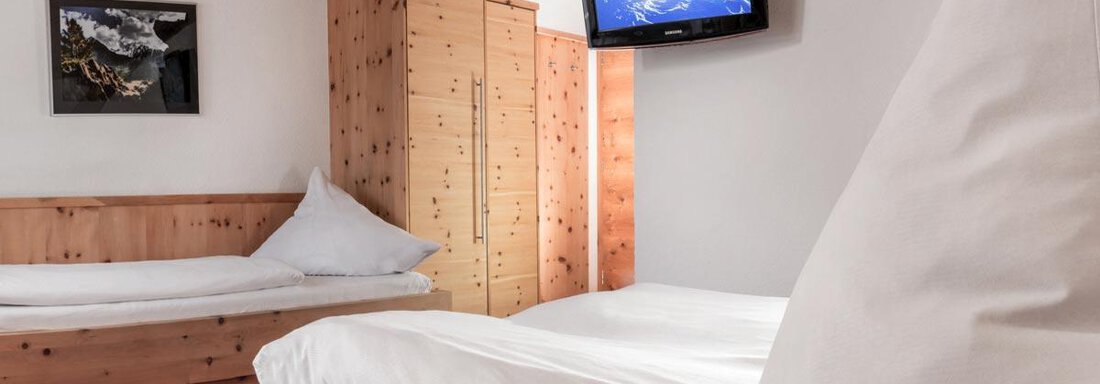 A bright room with a double bed and a single bed. A television hangs on the wall, and there is a wooden wardrobe and a large window. - Haus Tanja - Sölden