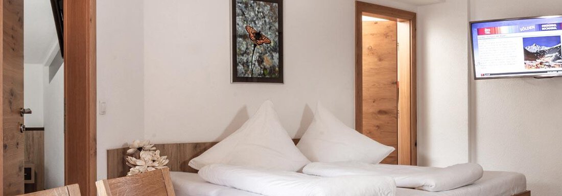 Wohnschlafzimmer A cozy bedroom with a large bed and white pillows. A picture hangs on the wall, and a television is visible. - Haus Tanja - Sölden