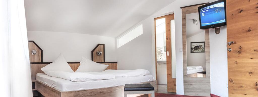 A modern hotel room with a double bed and a television. The walls are light, and the decor is simple and comfortable. - Haus Tanja - Sölden