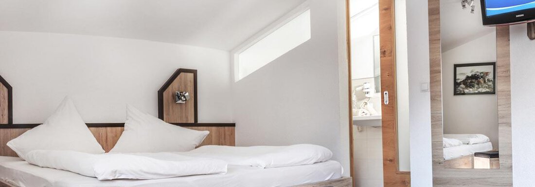 A modern bedroom with a large bed and fresh white bed linen. There is a television on the wall and a small table in the room. - Haus Tanja - Sölden