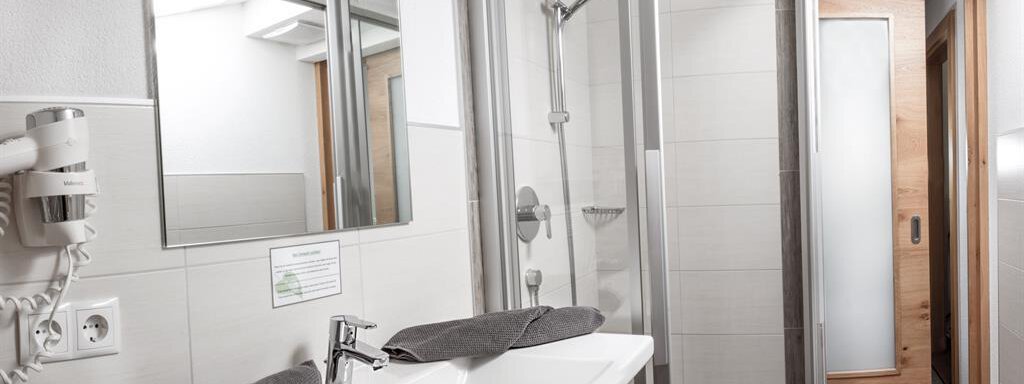 A modern bathroom with a sink and a shower. The walls are bright and the room is well lit. - Haus Tanja - Sölden