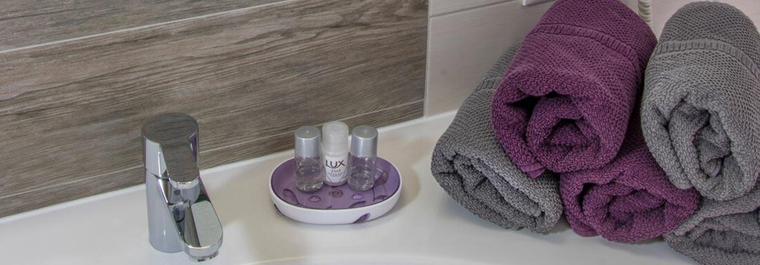 A modern bathroom with a sink and a faucet. Decorative towels in purple and gray, as well as personal care products, are laid on it. - Haus Tanja - Sölden