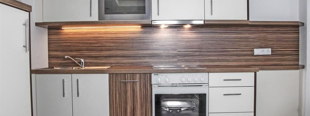 A modern kitchen with white and wood-colored cabinets. It is equipped with a stove, an oven, and a sink. - Haus Tanja - Sölden