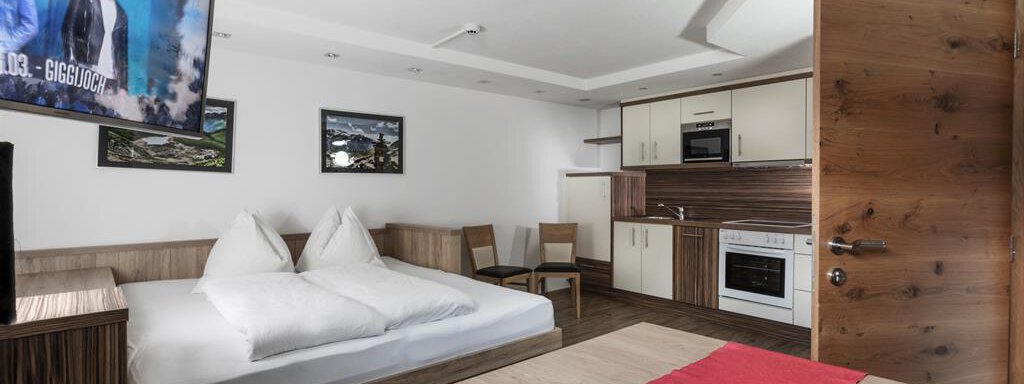 Wohnschlafküche A modern room with a double bed and a television. The kitchen is equipped, and there is a table with chairs. - Haus Tanja - Sölden