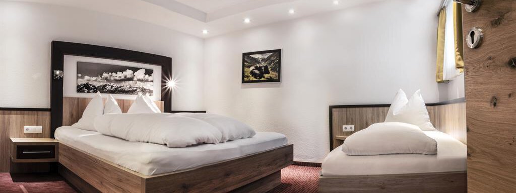 A bright and modern bedroom with a large double bed and a single bed. The walls are painted white and the floor has a red carpet. - Haus Tanja - Sölden
