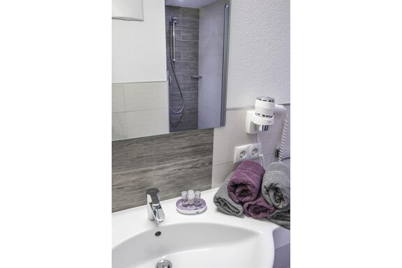 A modern bathroom with an elegant sink setup and a large mirror. Fresh towels and toiletries are on the shelf. - Haus Tanja - Sölden