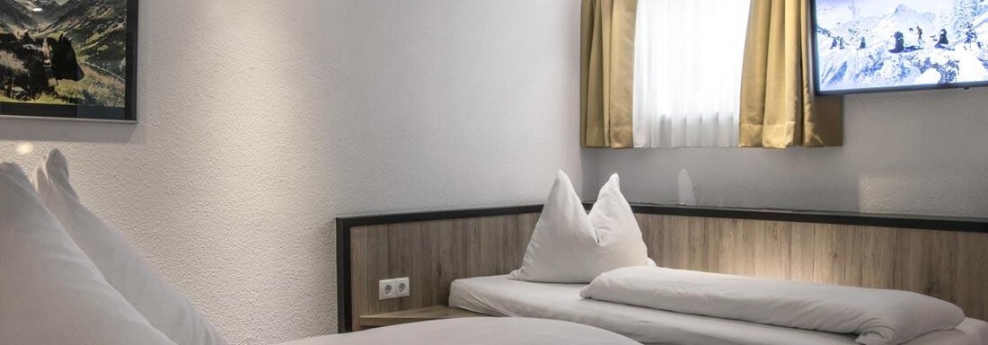 A cozy hotel room with two beds and a television. Bright walls and a window with curtains create an inviting atmosphere. - Haus Tanja - Sölden