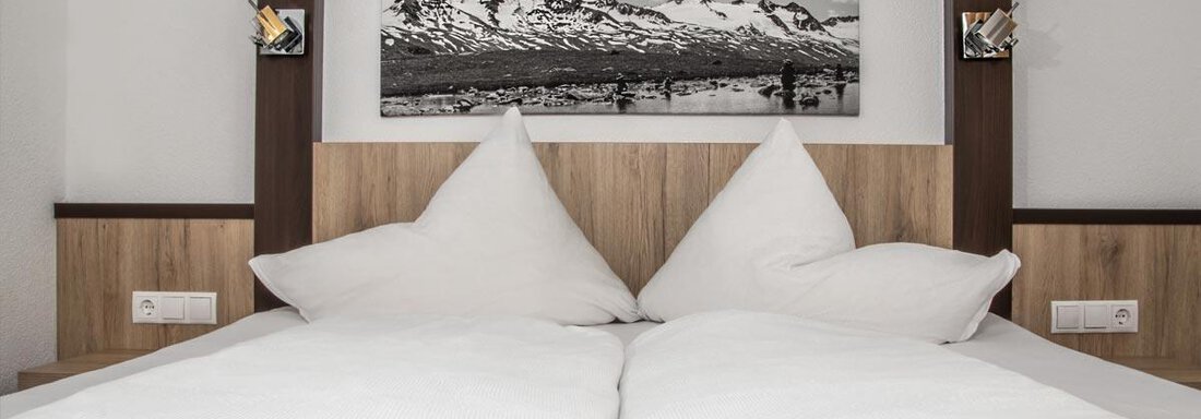 A cozy bedroom with a large bed and two pillows. On the wall hangs a picture of a mountain landscape. - Haus Tanja - Sölden