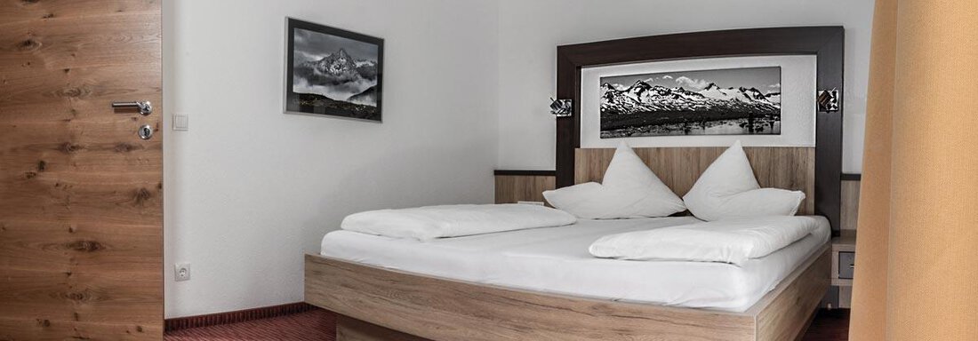 A cozy bedroom with a large bed and wooden details. The walls are bright, and there is a decorative picture of the mountains. - Haus Tanja - Sölden