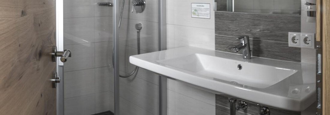 A modern bathroom with a shower and a washbasin. The walls are in light tones, and a wood detail is visible. - Haus Tanja - Sölden