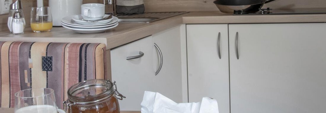 A modern kitchen with wooden paneling. On the table, there are breakfast ingredients such as muesli, milk, jam, and juices. - Haus Tanja - Sölden
