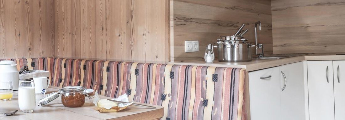 A cozy kitchen with wooden walls and a dining table. On the table are breakfast ingredients like jam and drinks. - Haus Tanja - Sölden