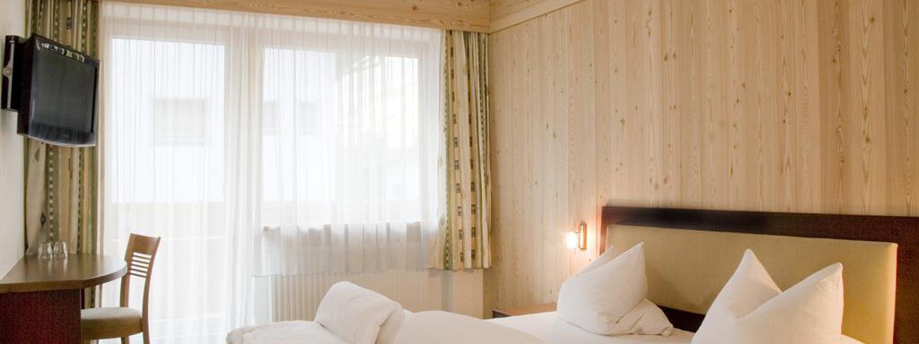 A comfortable hotel room with wooden panels and a double bed. The room is bright and friendly with a desk and a television. - Haus Tanja - Sölden