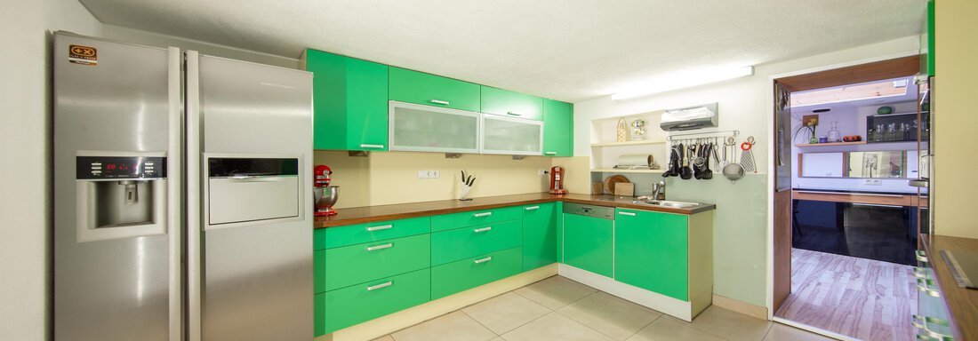 A modern kitchen with green cabinets and a large refrigerator. The room is bright and spacious, with tiled flooring. - Haus Valtelas - Sölden