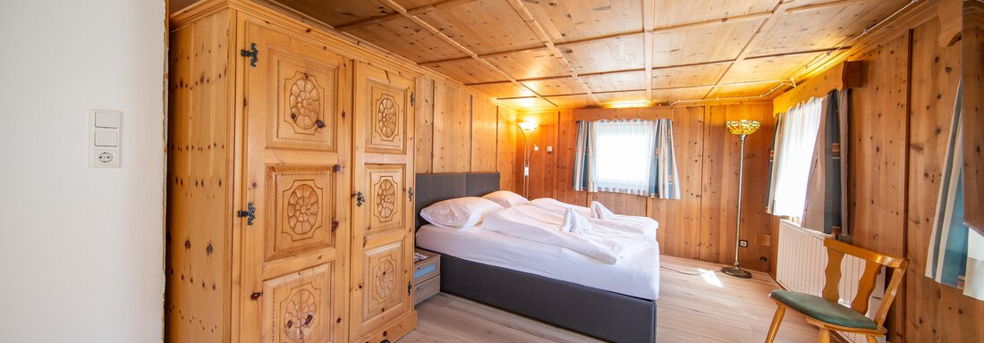 A cozy bedroom with wooden ceilings and furniture. The light gently falls through the window onto the bed and the chair. - Haus Valtelas - Sölden