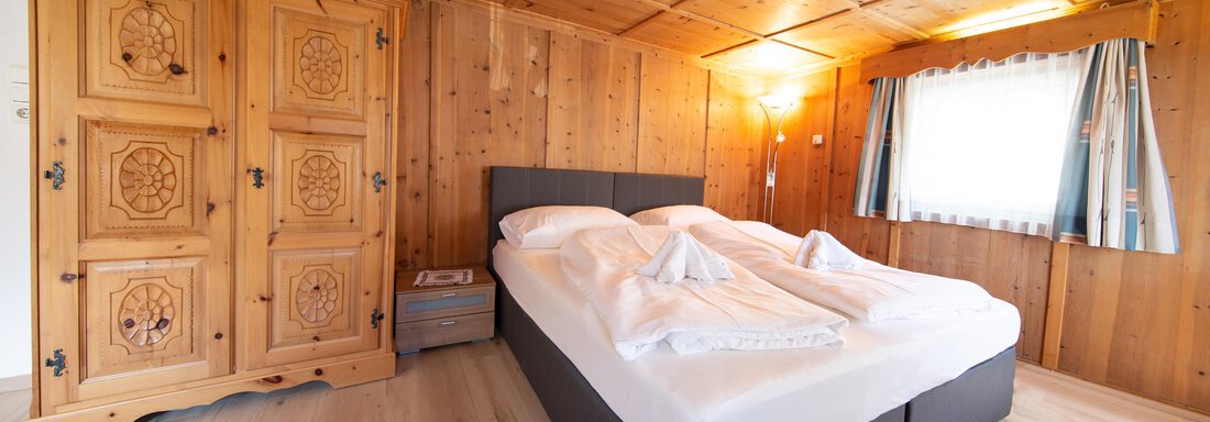 A cozy bedroom with a large bed and rustic wood decor. The windows let in plenty of daylight, creating an inviting atmosphere. - Haus Valtelas - Sölden
