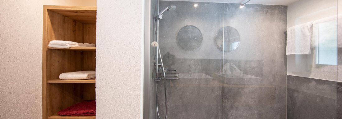A modern shower with transparent glass walls and modern fixtures. In the background, there is a wooden shelf with fresh towels. - Haus Valtelas - Sölden