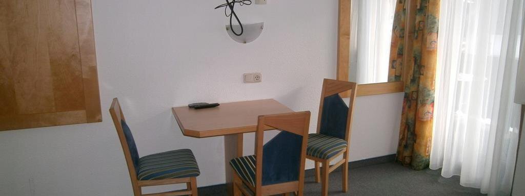 A simple room with a table and two chairs. A television hangs on the wall, and the window is decorated with curtains. - Hirschenhof - Sölden