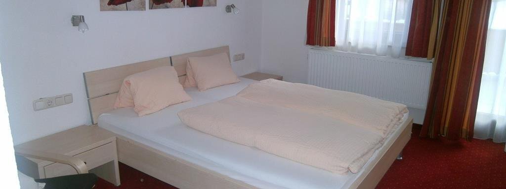 A simple bedroom with a double bed and two pillows. The walls are painted in light colors and there is a window with curtains. - Hirschenhof - Sölden